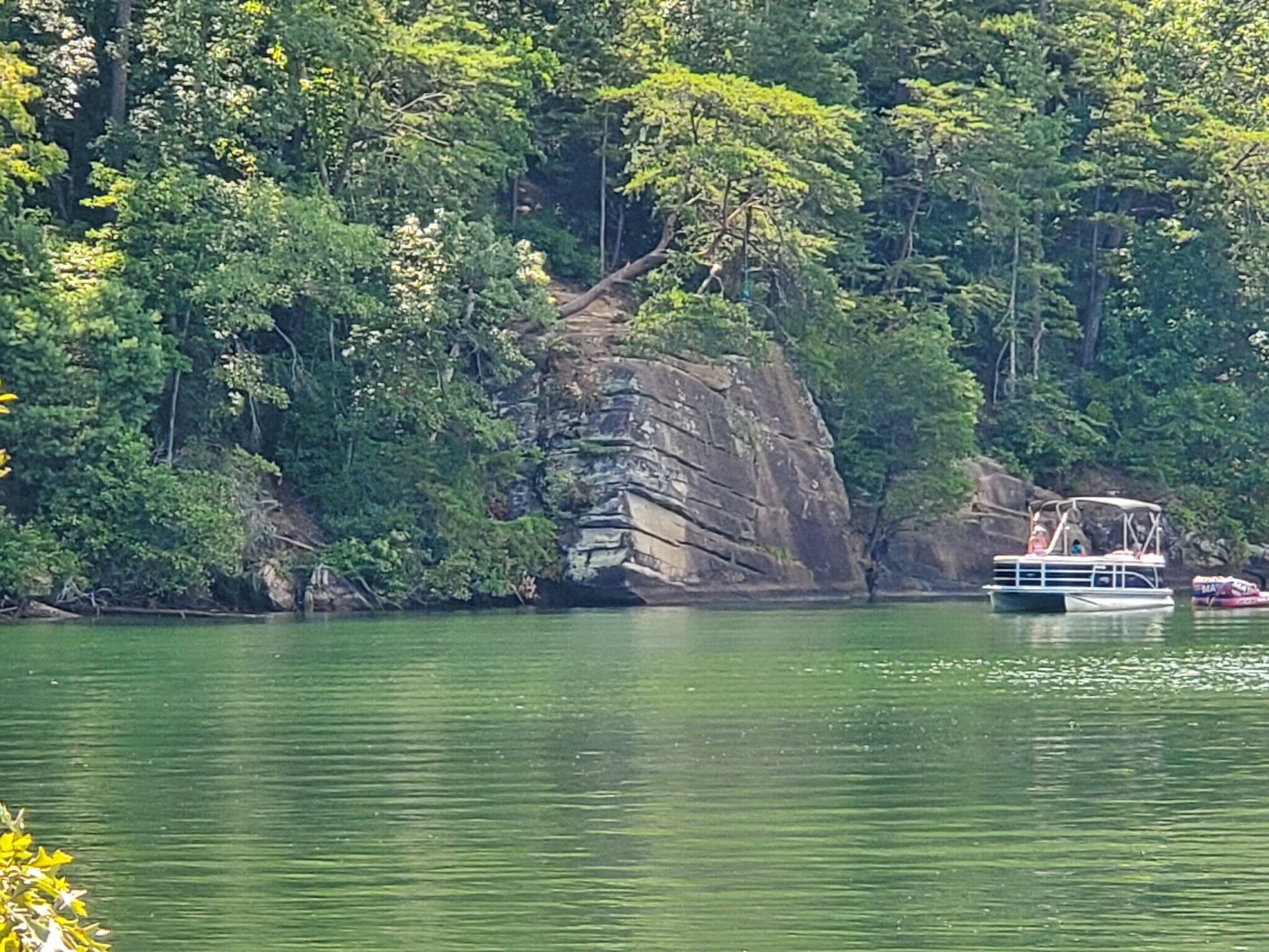 A large rock formation along the shore from which some kids were jumping into the lake.